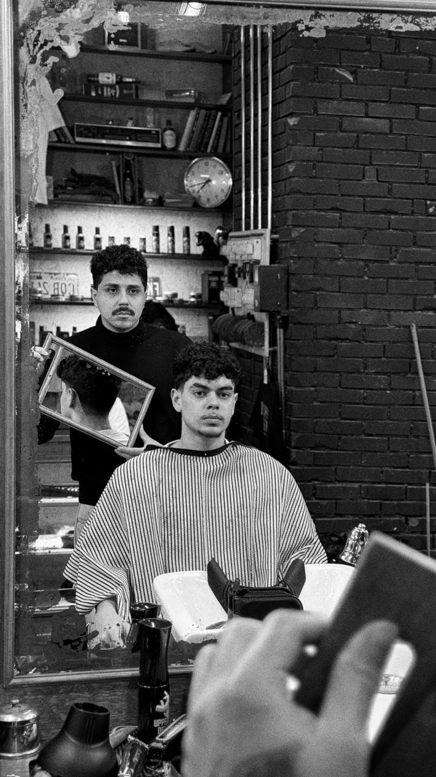 Barbeiro a mostrar o corte ao espelho a um cliente, na barbearia.